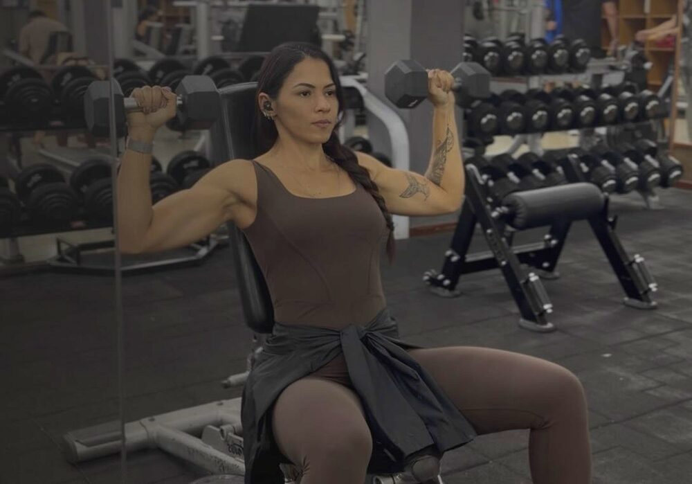 Carla treinando ombro com halteres numa academia